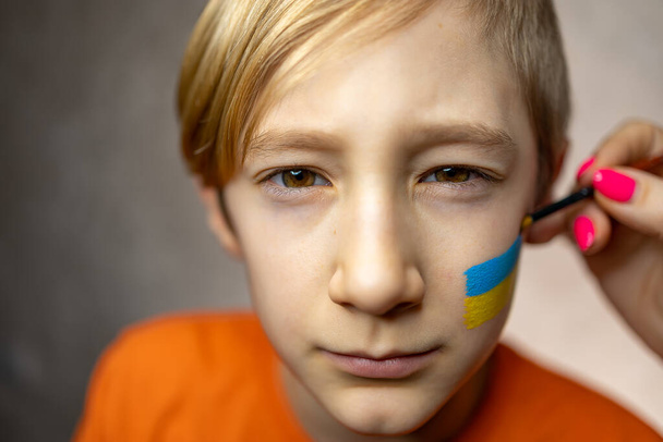 uma criança contra a guerra, um menino com uma bandeira pintada da Ucrânia em suas bochechas - Foto, Imagem