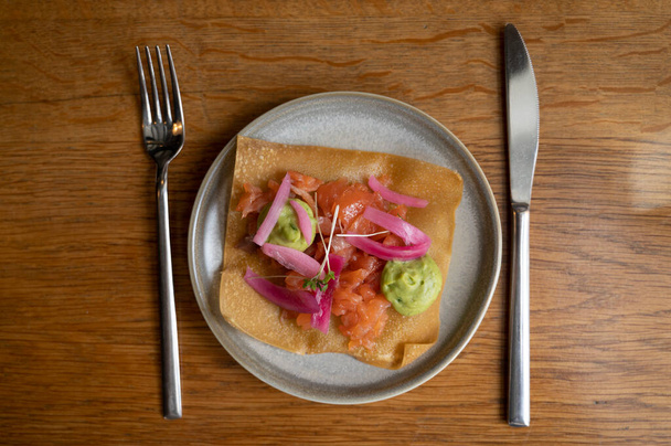 Mexican food, fried corn tortilla with smoked salmon, guacamole sauce and pink pickled onions close up - Photo, Image