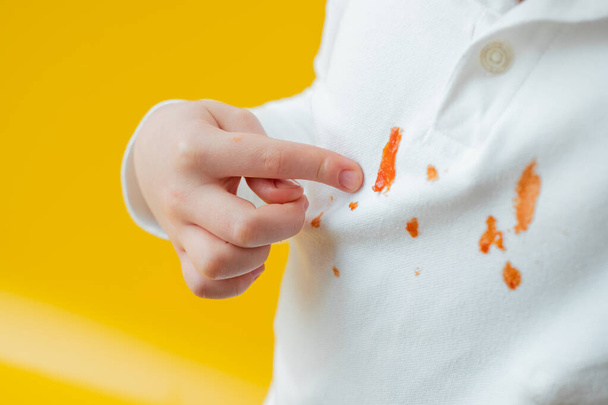 Dziecko wskazuje palcem na plamę keczupu na ubraniu. codzienna koncepcja plamy życia. Wysokiej jakości zdjęcie - Zdjęcie, obraz