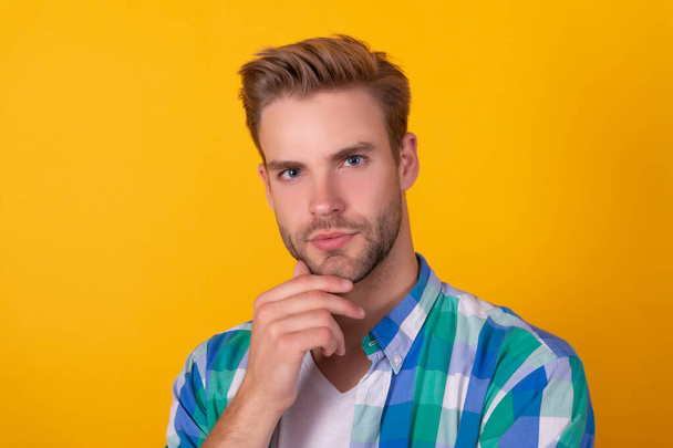 Handsome unshaven man portrait stroking chin with serious look yellow background, face - Foto, Bild