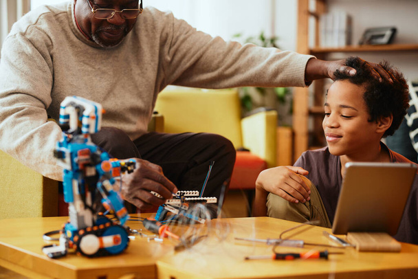 A grandfather showing his grandchild how to make a robot while sitting at home. - Photo, Image
