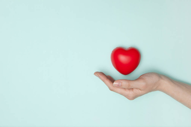 Gesundheits-, Medizin- und Wohltätigkeitskonzept - Nahaufnahme weiblicher Hände mit kleinem roten Herz. Flache Lage. - Foto, Bild