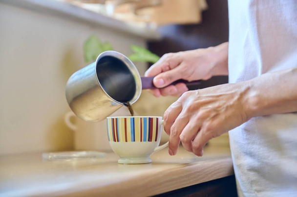 Close-up of a womans hands preparing coffee in an iron cezve. - Fotó, kép