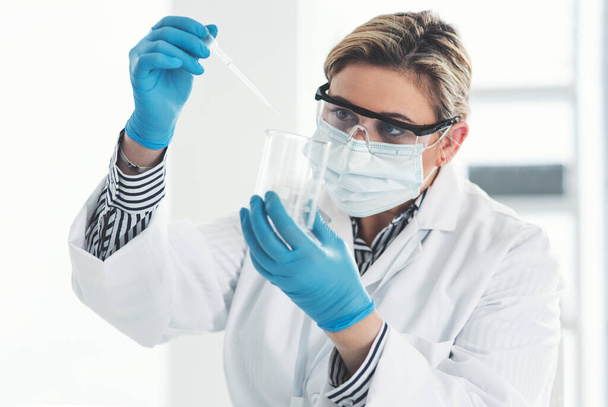 Just a few drops will do. Cropped shot of an attractive young female scientist dropping a liquid sample into a beaker while working in a laboratory. - Foto, imagen