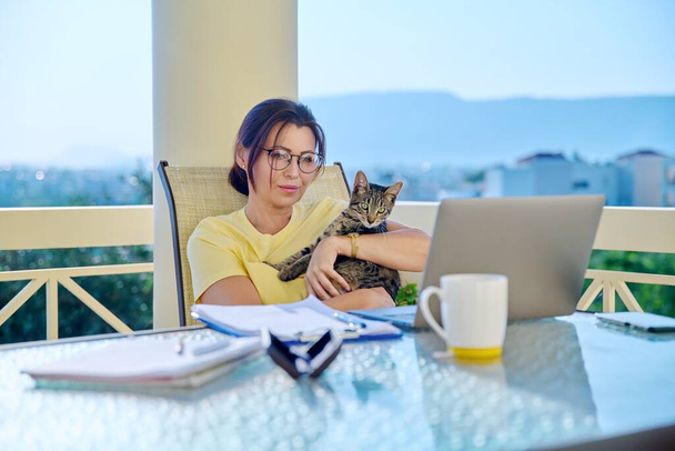 Middle-aged woman working at home with a cat in her arms. - Foto, imagen