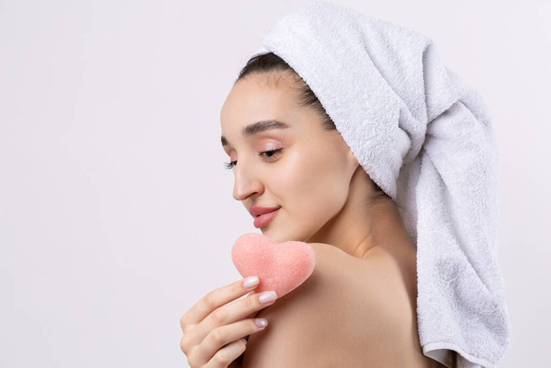 Beautiful girl with thick eyebrows and perfect skin at white background, towel on head, beauty photo. Holding a cosmetic pink heart sponge. - Φωτογραφία, εικόνα