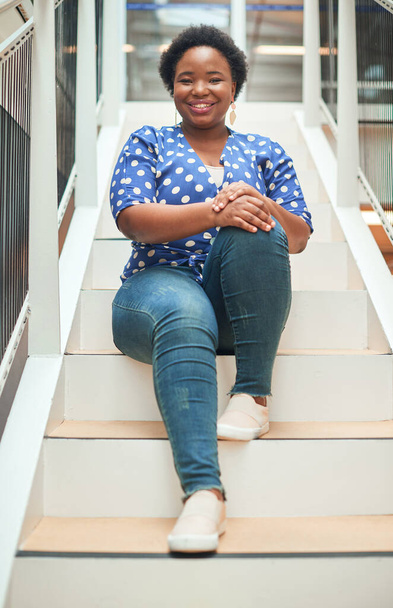 Пробираюсь к вершине шаг за шагом. Портрет уверенной молодой предпринимательницы, сидящей на ступеньках современного офиса. - Фото, изображение