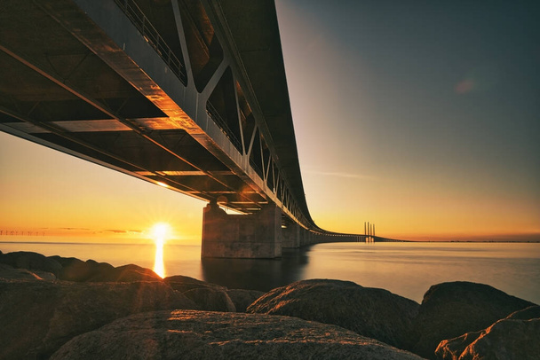日没時にデンマークとスウェーデンの間のオレンジ色の橋の長い露出 - 写真・画像