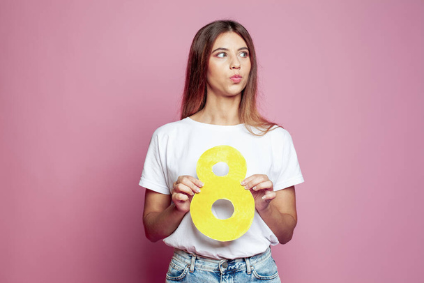 Young woman showing yellow number eight 8 on pink background with copy space - Φωτογραφία, εικόνα