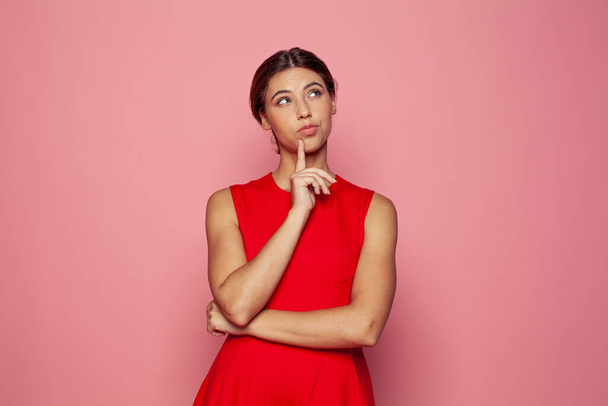 Dreamy pretty cute woman touching her chin thought choose decide solve problems dilemmas wearing fashionable outfit on pink background. Youth people portrait.  - Photo, Image
