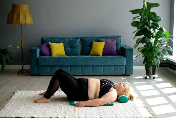 An overweight woman is lying on the floor on a massage mat with a needle pillow. Alternative treatment of back and neck pain as a consequence of obesity. Relaxing independent home massage. - Photo, Image