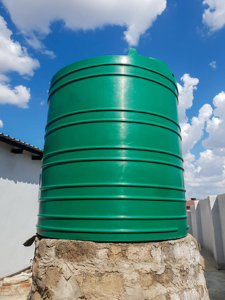 Великий зелений резервуар для води спирається на конструкцію з цегли та цементу з з'єднаними чорними пластиковими трубами та краном
 - Фото, зображення