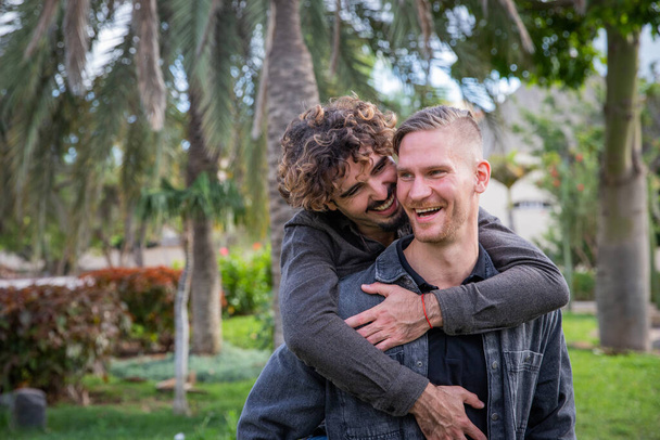 een gay paar heeft een moment van liefde samen een man tilt zijn vriend op zijn rug en ze lachen samen - Foto, afbeelding