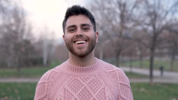 Hombre hispano mirando a la cámara y sonriendo mientras está parado al aire libre en el parque. - Imágenes, Vídeo