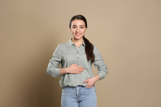 Happy healthy woman touching her belly on beige background - Photo, Image