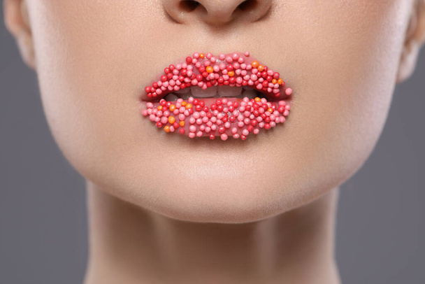 Young woman with beautiful lips covered confectionery sprinkles on gray background, closeup - Photo, image