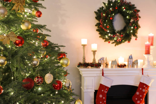 Beautifully decorated Christmas tree near fireplace in room. Interior design - Zdjęcie, obraz