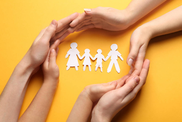 Parents and child protecting paper cutout of family on orange background, top view - 写真・画像