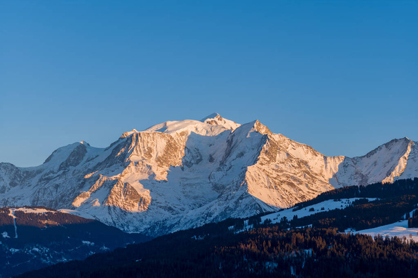 Αυτή η φωτογραφία τοπίου τραβήχτηκε στην Ευρώπη, στη Γαλλία, στο Rhone Alpes, στη Σαβοΐα, στις Άλπεις, το χειμώνα. Βλέπουμε το βουνό Mont Blanc στο ηλιοβασίλεμα, κάτω από τον ήλιο. - Φωτογραφία, εικόνα