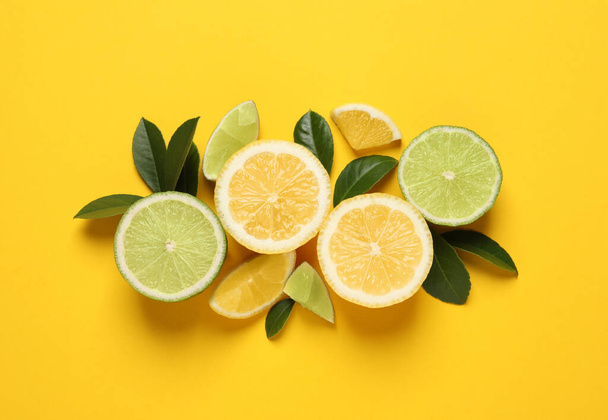 Fresh ripe lemons, limes and green leaves on yellow background, flat lay - Zdjęcie, obraz