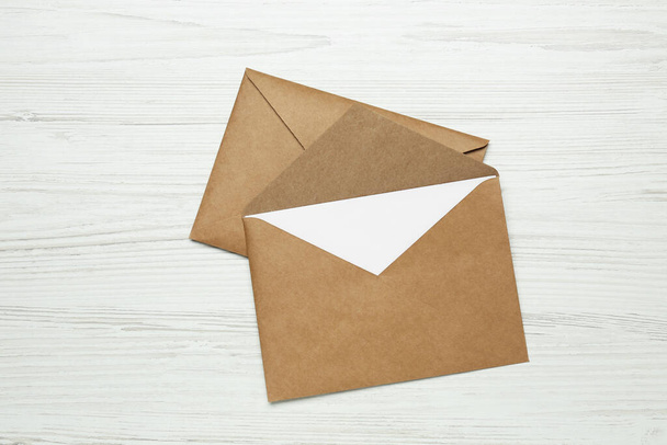 Envelopes with blank paper card on white wooden table, top view - 写真・画像