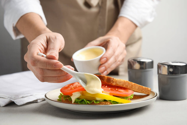Woman making sandwich with mayonnaise at grey table, closeup - Foto, afbeelding
