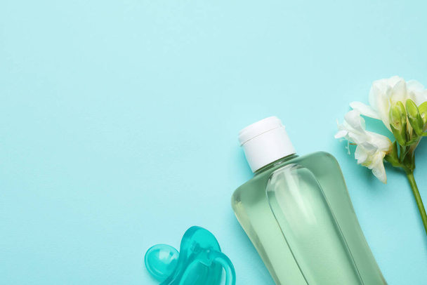 Bottle of baby oil, pacifier and blooming freesia on turquoise background, flat lay. Space for text - Foto, afbeelding