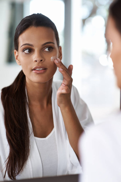 Good skin care is the foundation of her beauty routine. A lovely young woman applying makeup to her flawless skin in the mirror. - Foto, afbeelding