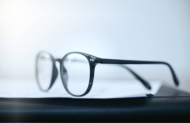 Halten Sie die Vision klar. Aufnahme einer Brille, die tagsüber auf einem Schreibtisch in einem leeren Büro liegt. - Foto, Bild
