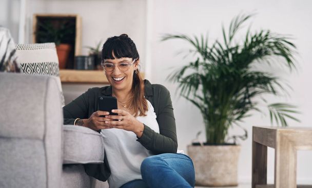 Technology keeps us connected. Cropped shot of an attractive young woman sitting in her living room alone and using her cellphone. - Foto, imagen