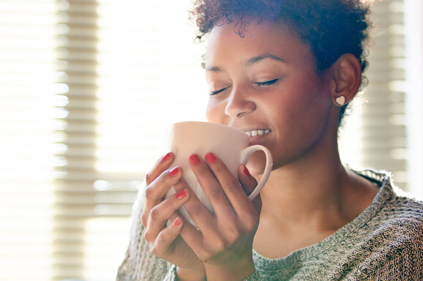 Onnellisuus on tuoreen kahvin tuoksu. Kasvatettu kuva nuoresta naisesta rentoutumassa kotona kupin kahvia. - Valokuva, kuva