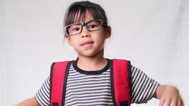 Cute uczennica noszenia okularów z plecakiem, ona ładny wygląd, uroczy i ciesząc się dobrym nastroju na białym tle w studio. Powrót do koncepcji szkoły - Materiał filmowy, wideo