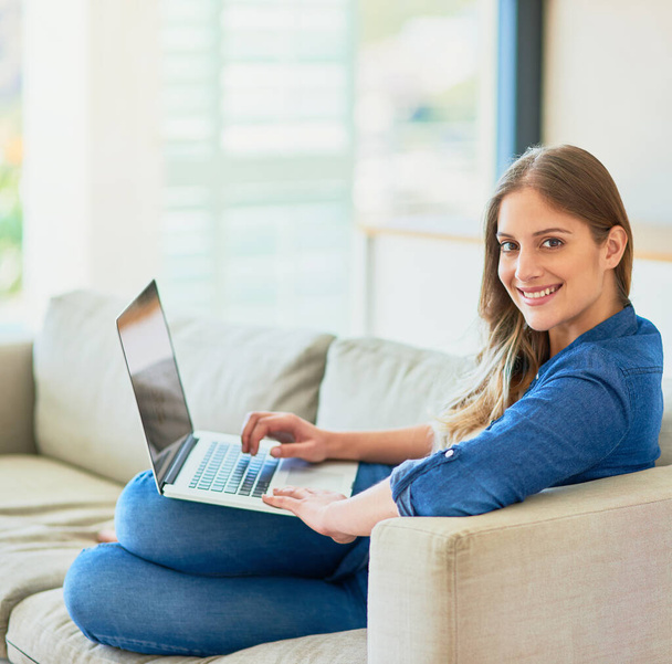Neem een pauze. Bladeren. Portret van een aantrekkelijke jonge vrouw met behulp van haar laptop terwijl ze thuis op de bank zit. - Foto, afbeelding