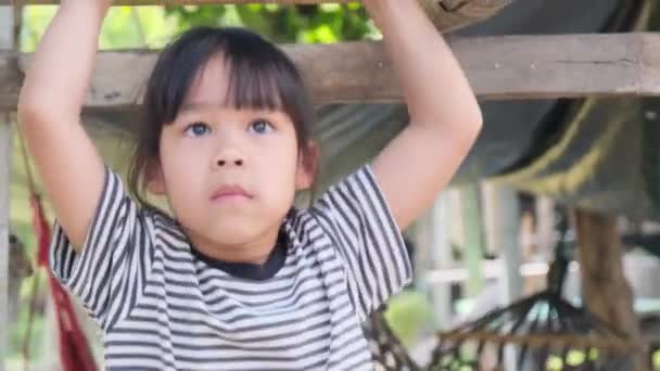 Cute Asian little girl wisi drewniany bar z rękami do ćwiczeń na podwórku placu zabaw. Aktywne dziecko wisi na drążku dwiema rękami. - Materiał filmowy, wideo