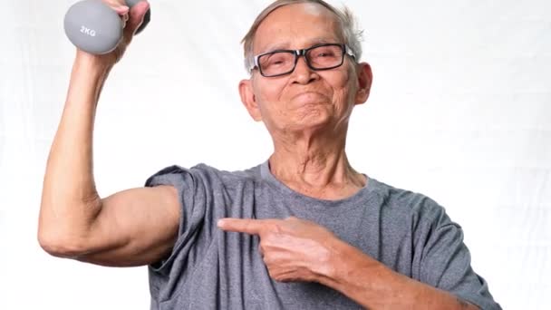 Ηλικιωμένος Ασιάτης σηκώνει αλτήρες και δείχνει μπράτσα. υγιεινός τρόπος ζωής - Πλάνα, βίντεο
