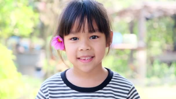 Cute little Asian girl z różowym kwiatem na uchu. Koncepcja szczęścia w dzieciństwie. - Materiał filmowy, wideo