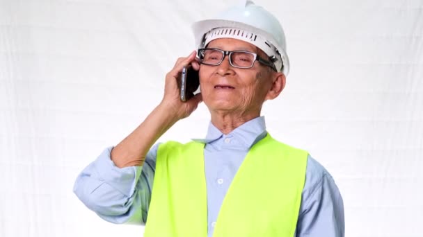 Старший инженер-архитектор в защитном жилете и шлеме обсуждает работу по телефону на белом фоне в студии. - Кадры, видео