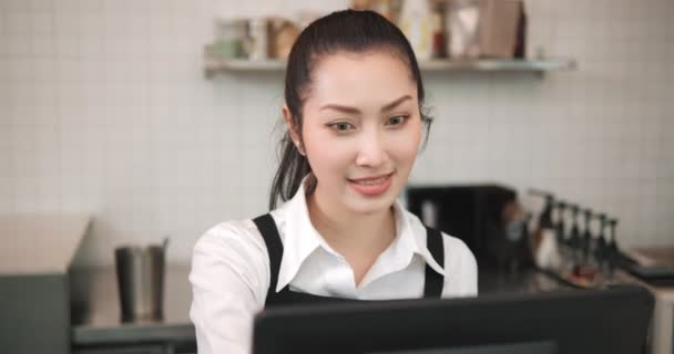 Mujer asiática empleada de cafetería barista trabajando en la cafetería. Cajero de camarera sonriente que pide café y panadería al cliente. Propietario de la pequeña empresa y concepto de trabajo a tiempo parcial - Imágenes, Vídeo