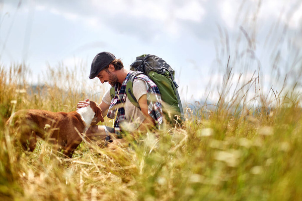 A young man is playing with his dog while walking a meadow on a beautiful sunny day. Hiking, nature, activity - Fotó, kép