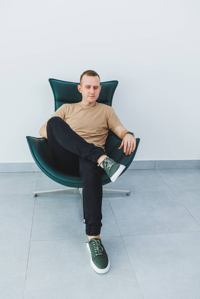 Stylish young man in a beige t-shirt and black trousers, a man in green leather casual sneakers. - Фото, зображення
