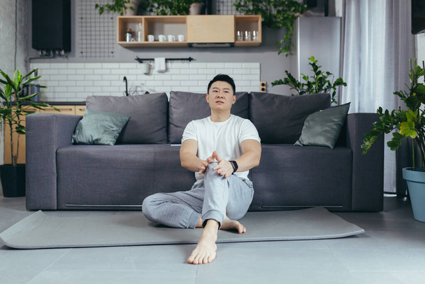 aziatische man in sportkleding lijden van knie pijn thuis - Foto, afbeelding
