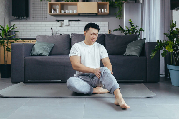 Asian Man in sportswear suffering from knee pain at home - Foto, afbeelding