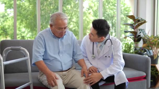 Aziatische man arts dragen witte lab jas controleren knie van oudere man patiënt zitten op de bank, ouderen gezondheidszorg support concept. - Video
