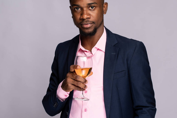 portrait of a young african american man in a suit with a glass of champagne against a pink background - Fotó, kép