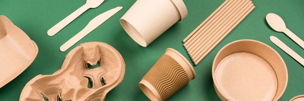 Banner with eco-friendly tableware - kraft paper utensils on green background. Paper cups and containers. Street food paper packaging, recyclable paperware, zero waste packaging concept. Mockup, flat lay - Фото, изображение
