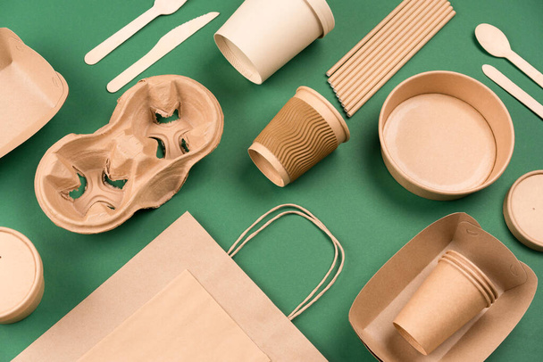 Eco-friendly tableware - kraft paper utensils on green background. Paper cups and containers, wooden cutlery. Street food paper packaging, recyclable paperware, zero waste packaging concept. Mockup, flat lay - Photo, Image
