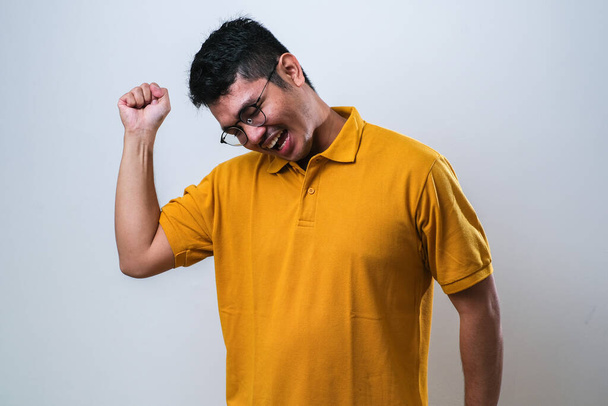 asiático hombre mostrando feliz excitado expresión con apretado puño sobre blanco fondo - Foto, imagen