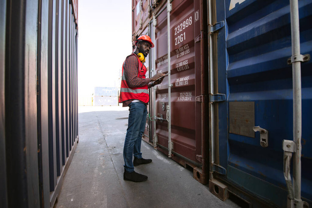 Afrikanischer männlicher Arbeiter hält Tablette in der Hand und kontrolliert die Verladung von Frachtcontainern vom Frachtschiff für den Import-Export. - Foto, Bild