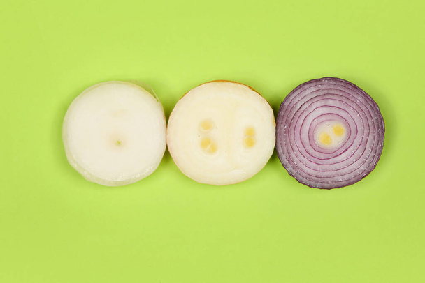 Three sliced onion of different colors (red, yellow and white) isolated on green background. High resolution photo. Full depth of field. - Photo, Image