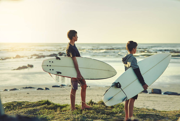 Mają przypadek gorączki surfingowej. Strzał dwóch młodych braci trzymających deski surfingowe patrząc w stronę oceanu. - Zdjęcie, obraz